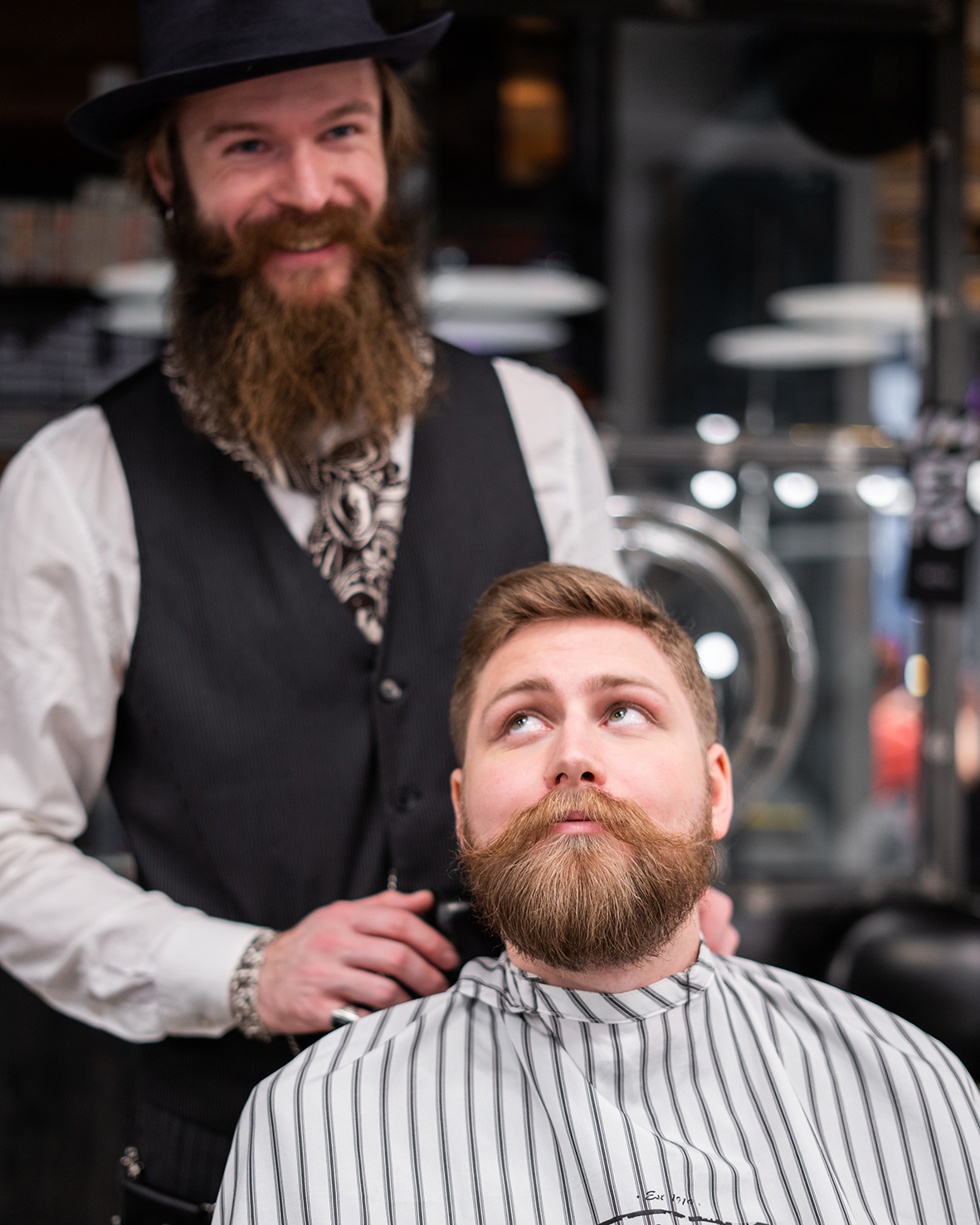 A client sits in the barber’s chair and his beard has been groomed with the help of the beard balm. Behind him stands his barber.